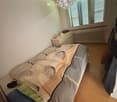 Cozy bedroom with a single bed, nightstand, radiator, and coat rack. The bed is made with a patterned duvet and pillows, and a decorative item hangs from the ceiling.