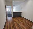 Empty hallway with polished wooden flooring, white walls, and a reception area visible in the background.