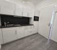 Modern kitchen with white cabinets, black countertops, a sink, and a microwave. The floor is made of wood tiles.