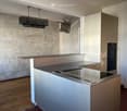Kitchen. Modern kitchen with white and grey cabinets, stainless steel countertop, built-in oven, and a decorative bull sculpture on the wall. The space features a wooden floor and a sleek chandelier hanging from the ceiling.