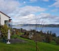 A serene garden area with a bench and umbrella, overlooking a scenic lake and distant hills.