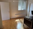 Empty room with wooden flooring, white walls, a window with blinds, a radiator, and a small table with a monitor and a tray.