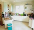 Bright, modern kitchen with white cabinets, granite countertops, and various appliances including a microwave, coffee maker, toaster, and oven. The space features a sink with a faucet, a wooden cutting board with bread, and several potted plants on the co