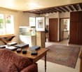 Living room with a red sofa, wooden coffee table with books, fish tank, and a patterned rug on the floor. The room features wooden beams on the ceiling and large windows letting in natural light.