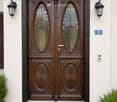 Ornate wooden double doors with decorative glass panels, flanked by black wall-mounted lanterns and a house number sign.