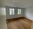 Empty room with wooden flooring and white walls, featuring two windows and a door.