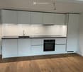 Modern kitchen with light grey cabinets, a black countertop, a sink, and an oven. The floor is made of light wooden planks.