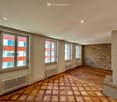 Empty room with wooden flooring, large windows, radiators, and exposed stone wall.