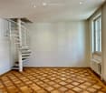 Spacious hallway with a modern spiral staircase, wooden herringbone floor, white walls, and recessed lighting.