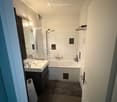 Modern bathroom with white tiles, a sink, bathtub, mirror, and shower area. Includes a towel on the floor and toiletries on the sink.