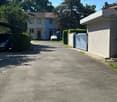 Driveway leading to a two-story house with a garage on the left and a gated entrance on the right, surrounded by greenery and trees.