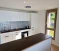Modern kitchen with white cabinets, dark countertop, sink, oven, and coffee maker. Features a large window with a view of greenery outside.