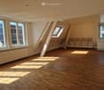 Empty attic room with wooden flooring, large windows, and skylights allowing natural light to fill the space.