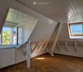 Bright, empty attic room with wooden floors, white paneled walls, and multiple windows offering natural light and scenic views.