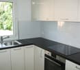 Modern kitchen with white cabinets, black countertops, stainless steel sink, induction cooktop, and built-in oven.