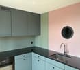 Modern kitchen with grey and mint green cabinets, black countertop, stainless steel sink, and a built-in oven.