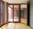 Empty hallway with wooden flooring, large glass doors leading to a balcony area, and neutral-colored walls.