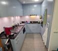 Modern kitchen with light grey cabinets, black countertops, stainless steel sink, coffee maker, and various appliances. Includes a ladder and dish rack in the corner.