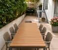 Garden / Outdoor Area. A modern outdoor dining area with a wooden table and grey chairs, surrounded by greenery and potted plants.