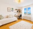 Cozy bedroom with a sofa bed, desk, bookshelf, and large windows offering a scenic view.