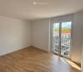 Empty room with wooden flooring, white walls, and a sliding glass door leading to a balcony.