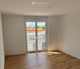 Empty room with wooden flooring, white walls, and a large sliding glass door leading to a balcony.