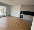 Empty kitchen with light wooden flooring, white cabinets, and a black countertop. Large window with a view of the outdoor area.