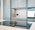 Modern kitchen with sleek, light-colored cabinets, a smooth countertop, and an induction cooktop. The space is well-lit with recessed lighting and features a minimalist design.