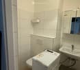 Modern bathroom with white tiles, a toilet, a sink with a mirror, a washing machine, and a light fixture.