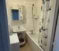 Compact bathroom with a bathtub, sink, mirror, and private washing machine. Features a shower curtain and a round ceiling light.