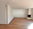 Empty room with wooden flooring, white walls, and a fireplace with a wooden bench.