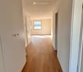 Empty hallway with wooden flooring, white walls, and several doors leading to other rooms.
