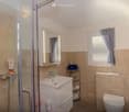 white sink, shower area with glass door, toilet, shelves, tiles