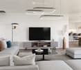 Modern living room with a grey sectional sofa, coffee table, ottoman, television, floor lamp, and a dining area with a table and chairs.