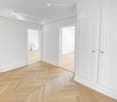 Empty hallway with white walls, wooden herringbone flooring, and several white doors.