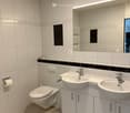 modern bathroom with white tiles, two sinks, toilet, mirror, and towel rack