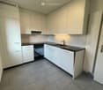 Modern kitchen with white cabinets, black countertops, and grey tiled flooring. Features include a sink, faucet, and oven.