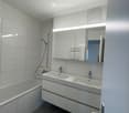 Modern bathroom with white tiles, a bathtub, a double sink with a large mirror, and a showerhead visible.