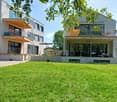 Modern two-story house with balconies, patio furniture, and a well-maintained lawn.