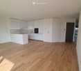 Empty kitchen with white cabinets, wooden flooring, and a black door leading to another room.