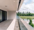 Modern balcony with large glass windows, glass railing, and scenic view of a park and water body.
