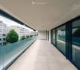 Modern balcony with large glass railings, tiled floor, and expansive city view.