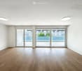 Empty room with wooden flooring, white walls, large glass sliding doors leading to a balcony, and recessed ceiling lights.