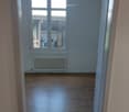 Empty room with wooden flooring, white walls, a radiator, and a large window with a view of an outdoor area.