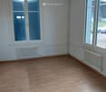 Empty room with light wooden flooring, white walls, and large windows with blinds. Radiators are visible along the walls.