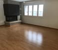 Empty room with wooden flooring, fireplace, and large windows with a view of buildings.