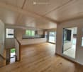 Open-plan space with wooden flooring, exposed wooden ceiling beams, and a staircase leading to another level. The area includes a kitchen with cabinets and a sink, and large windows and sliding glass doors provide natural light and access to an outdoor ar