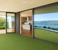 Bright, modern room with green carpeting, large glass sliding doors opening to a balcony, and a visible kitchen area with white cabinets and stainless steel appliances.