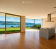 Modern kitchen with wooden flooring, large windows offering scenic views, kitchen island, and range hood.
