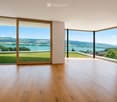 Empty room with wooden flooring, large glass sliding doors, and scenic view of a lake and landscape.